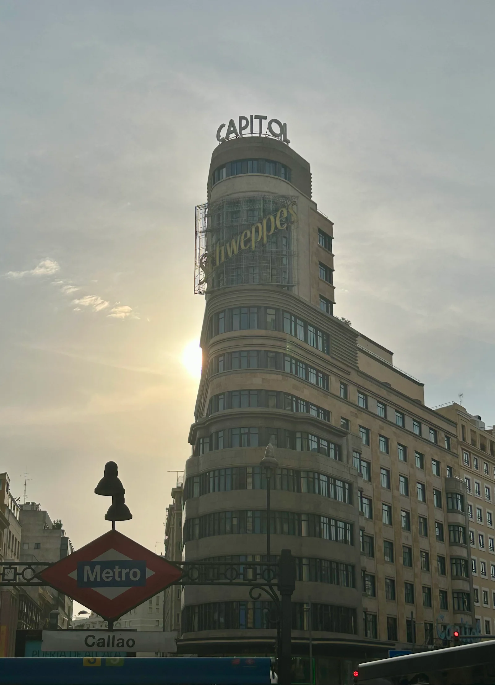 Vista desde la Plaza de Callao en Madrid, con el letrero del metro en primer plano y el Edificio Capitol recibiendo los últimos rayos del atardecer